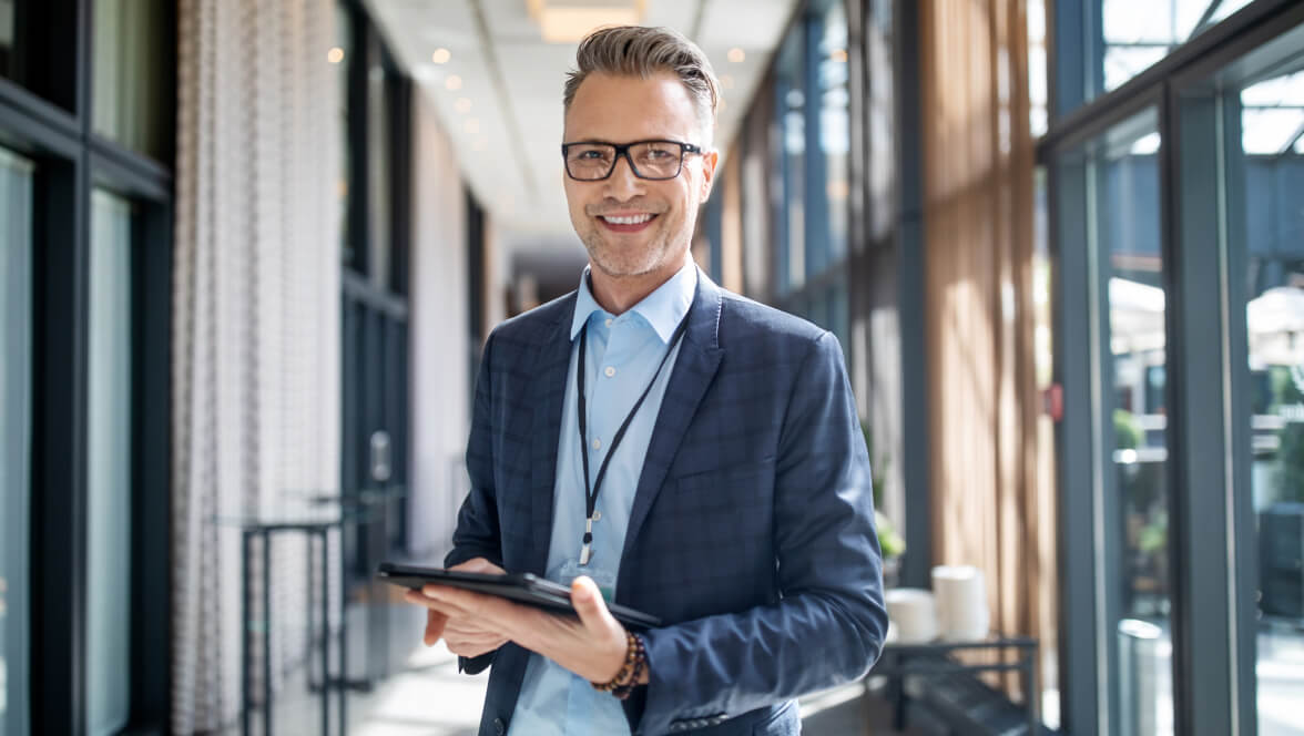 una persona que lleva un traje con gafas sosteniendo una tablet y sonriendo