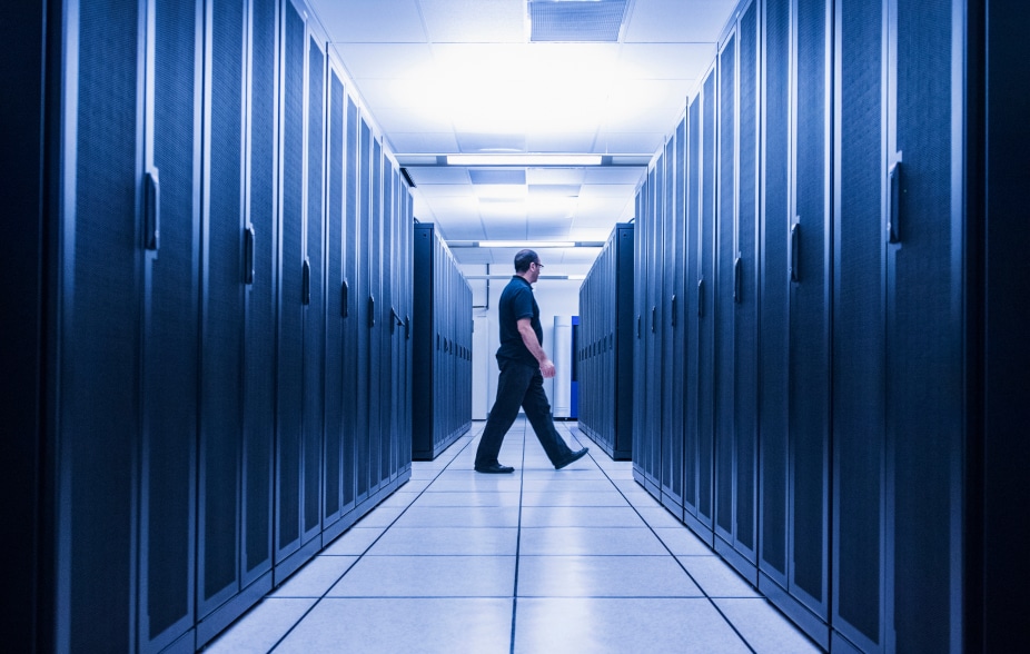 Homme en uniforme de personnel de sécurité qui marche entre les allées de matériel informatique d'un data center sécurisé.