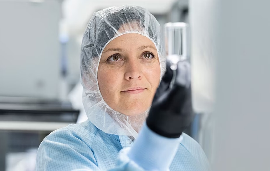 Femme en tenue de bloc opératoire qui tient devant elle un conteneur d'échantillon dont elle inspecte le contenu.