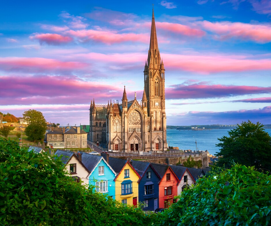 Un cielo colorato solcato da nuvole fa da sfondo a un quartiere di Cork, con case colorate e un imponente campanile della chiesa.