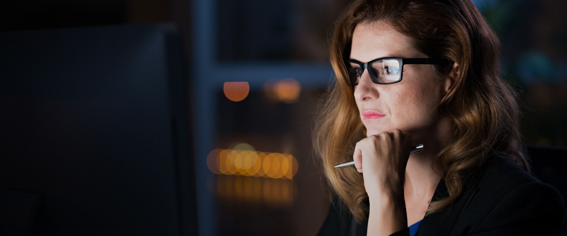 person wearing glasses looking at the computer and holding pen in the hand