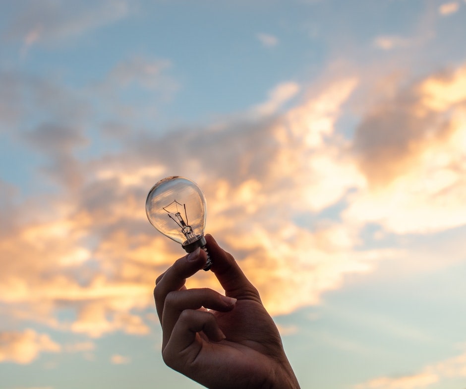 hand holding lightbulb backlit by a cotton candy sky