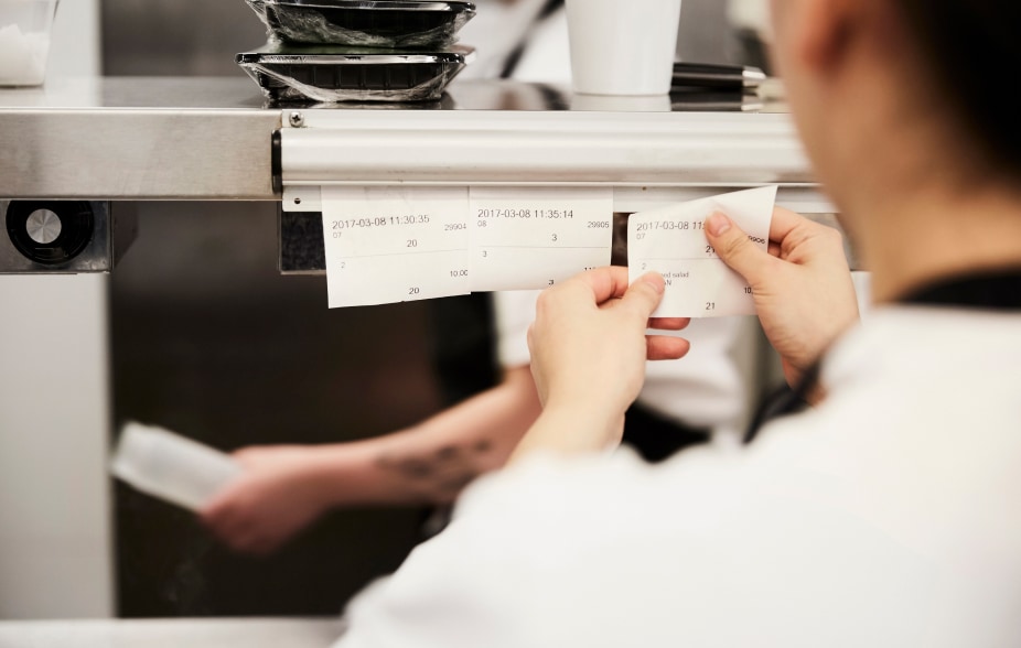 A chef in a restaurant pins order tickets to a call board.