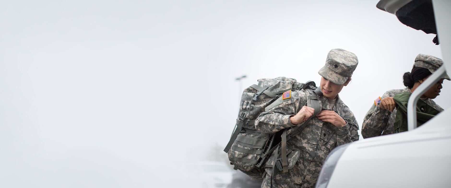 Two Military people trying to keep their luggage in the trunk